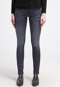 Vaqueros ajustados en denim de lavado oscuro, con un acabado desvaído y un ligero efecto de desgaste. Combinados con zapatos negros sin cordones con cremalleras doradas.