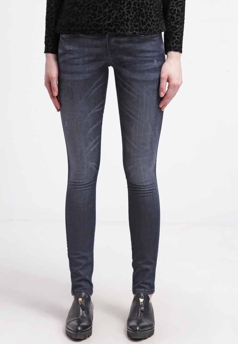 Vaqueros ajustados en denim de lavado oscuro, con un acabado desvaído y un ligero efecto de desgaste. Combinados con zapatos negros sin cordones con cremalleras doradas.