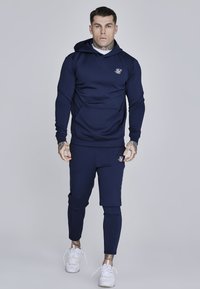 Felpa blu navy con cappuccio e pantaloni jogger abbinati in un design aderente, realizzati in un tessuto liscio con un logo discreto sul petto e sull'anca.