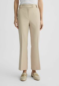 Pantaloni beige su misura con gamba dritta, dettaglio della piega e vita elastica. Il tessuto appare liscio con una leggera lucentezza; indossati con mocassini crema chiaro.
