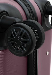 Primer plano de una maleta rígida color marrón con ruedas giratorias negras dobles y cremallera visible a lo largo del borde.