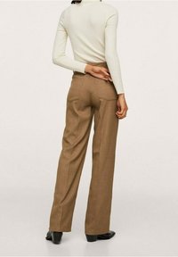 Brązowe spodnie o wysokim stanie z prostą nogawką, dwoma tylnymi kieszeniami i teksturowanym materiałem. Noszone z dopasowanym białym topem z długim rękawem.