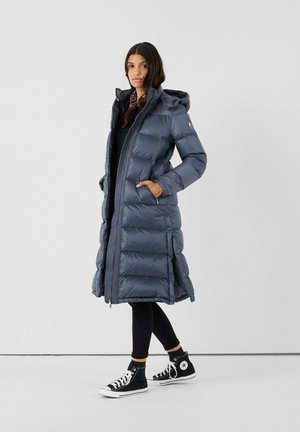 Giacca a vento imbottita di un grigio scuro con zip frontale, cappuccio e tasche laterali; presenta un design lungo e aderente con texture trapuntata e dettagli in bottone.
