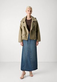 Olivengrønn skinnimitasjons motorsykkeljakke med skulderklaffer, tettsittende brun topp og mørk denim maksi-skjørt med detaljert søm foran.