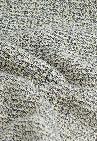 Gros plan sur un tissu tissé texturé avec des fils beige, noirs et blancs créant une surface en relief et à motifs.