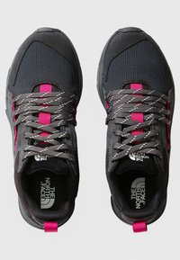 Un par de zapatillas The North Face en negro y gris con detalles en rosa y cordones reflectantes grises, vistas desde arriba sobre un fondo blanco.