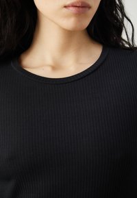 Μαύρο ριχτό μπλουζάκι με στρογγυλή λαιμόκοψη, που επιδεικνύει λεία υφή και υποχρεωτικές κάθετες γραμμές. Χωρίς ορατές κλείσεις ή μοτίβα.