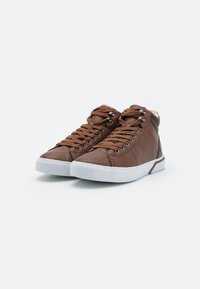Brown leather high-top sneakers with textured sides, prominent laces, and white rubber soles. Accented with metal eyelets and soft lining.
