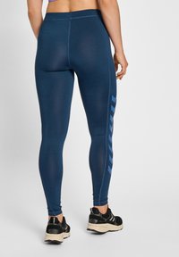 Marinblå leggings med åtsittande passform och texturerad yta, med en blå sidostrimma och kontrasterande sömmar. Svarta träningsskor fulländar looken.