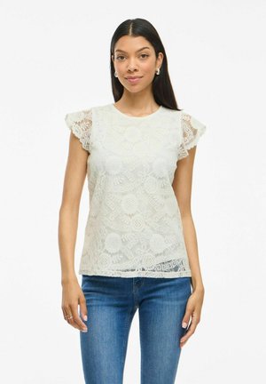 Lace blouse in light green featuring a floral pattern, short ruffled sleeves, and a scalloped hem. Paired with blue denim jeans.