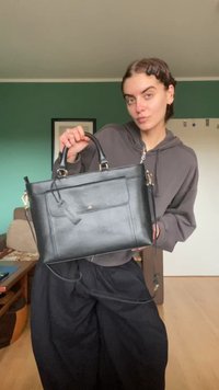 Melna ādas rokassoma ar strukturētu formu. Tai ir priekšējais kabata, augšējie rokturi un noņemams plecu siksna. Ar teksturētu apdari.