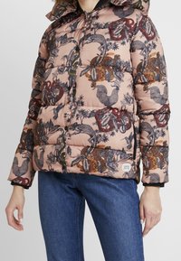Chaqueta acolchada en rosa suave con intrincadas ilustraciones oscuras de animales y plantas. Presenta una capucha, cierre de cremallera y detalles en las mangas.