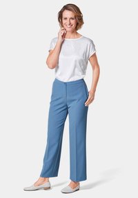Helle blaue, taillierte Hose mit einem Knopfverschluss vorne, kombiniert mit einer weißen Bluse mit kurzen Ärmeln und dekorativen Strasssteinen.