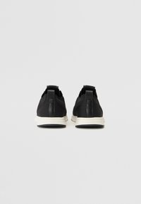 Baskets de sport noires avec une tige en mesh, des accents en cuir, une semelle en caoutchouc blanche et une languette au talon pour un enfilage facile.