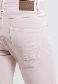 Jeans rose clair en denim, dotés d'une poche arrière unique et d'un label en cuir marron avec une inscription en relief.