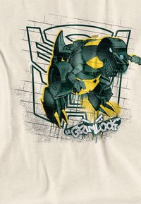Graphic t-shirt with a beige background featuring a black and yellow robot dinosaur design, splattered paint effect, and stylized text "Grimlock."