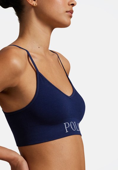 Námořnicky modrý žebrovaný bralette s hlubokým výstřihem do V, tenkými ramínky a páskem s bílým logem "POLO". Měkká látka a elastický pásek.