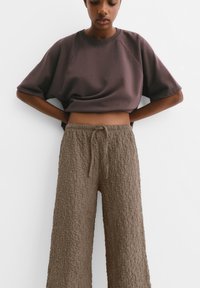 Felpa corta marrone scuro con maniche corte abbinata a pantaloni larghi marrone chiaro con texture, dotati di cintura elastica e cordoncino.