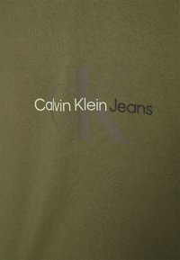 Olivegrønn bomull t-skjorte med teksten "Calvin Klein Jeans" i hvit og mørkegrå, med en glatt tekstur og avslappet passform.