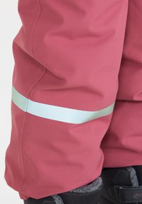 Roze waterdichte broek met reflecterende mintgroene streep langs het onderbeen, gemaakt van een gestructureerde, duurzame stof en verstelbare laarzenmanchetten.