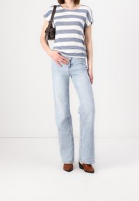 Pruhovaná modro-bílá košile s krátkým rukávem, světle modré rozšířené džíny a hnědé kotníkové boty na podpatku, s malou černou kabelkou přes rameno.