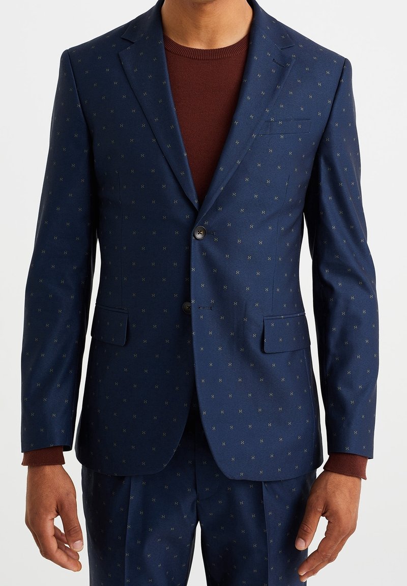 Navy blazer with subtle polka dot pattern, notched lapels, two buttons, and two front pockets. Worn over a maroon crewneck sweater.