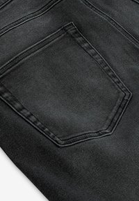 Schwarzer Denim-Stoff mit einer standardmäßigen Gesäßtasche, die einen doppelt genähten Rand und eine dezente Textur aufweist, entworfen für Haltbarkeit und Stil.