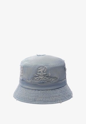 Denim bucket hat vaaleansinisena, jossa on kuluneet reunat. Varustettu päähineen ympärillä olevalla solidilla nauhalla ja päällä on pääkallon brodeeraus. Teksturoitu kangas.