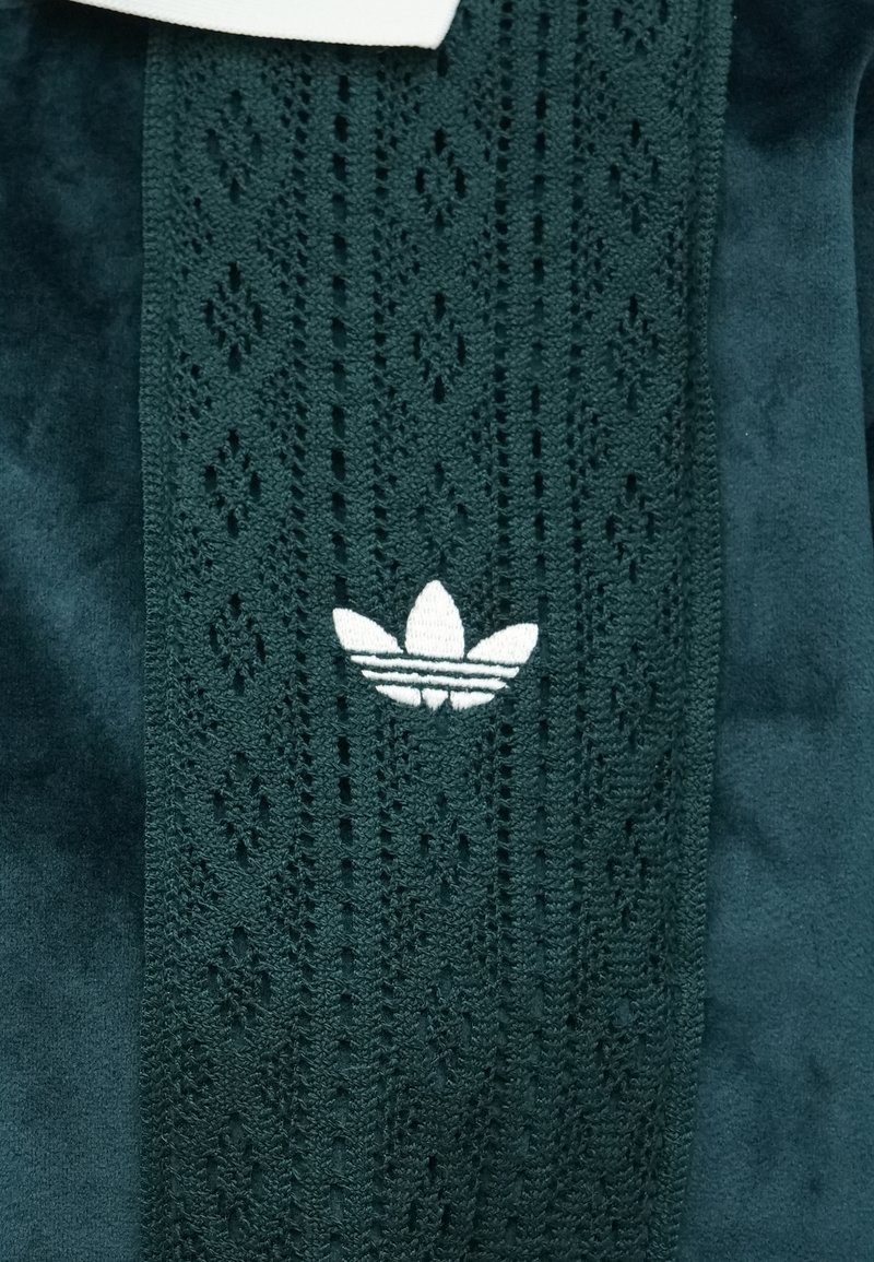 Dark green fabric with textured middle panel featuring diamond patterns, accented by a white embroidered three-leaf logo. Soft suede finish.