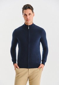 Granatowy sweter na zamek błyskawiczny z wysokim kołnierzem, dopasowany fason, długie rękawy i boczne kieszenie. Miękka tekstura z gładkim wykończeniem dzianiny.