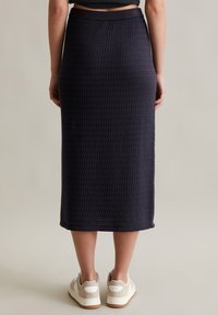 Navyblaue Midikleid mit strukturiertem Muster, tailliertem Bund und seitlichen Schlitzen. Kombiniert mit hellfarbenen Sneakers.