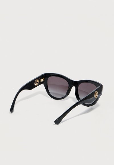 Μαύρα γυαλιά ηλίου σε σχήμα γάτας με σκουρόχρωμους φακούς με διαβάθμιση και χρυσές κυκλικές λεπτομέρειες λογότυπου στους βραχίονες, τοποθετημένα σε λευκό φόντο.