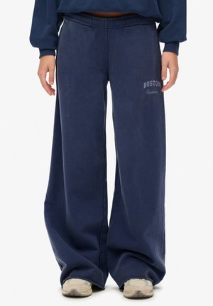Pantalons de survêtement larges bleu marine en tissu doux avec une taille élastique, portant l'inscription "BOSTON" en bleu clair sur le côté gauche.