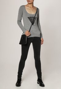 Haut à manches longues gris avec un col rond, orné d'un design graphique triangulaire noir incluant du texte ; associé à un jean skinny noir et des bottines.