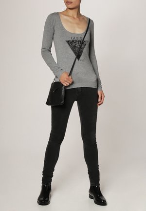 Haut à manches longues gris avec un col rond, orné d'un design graphique triangulaire noir incluant du texte ; associé à un jean skinny noir et des bottines.