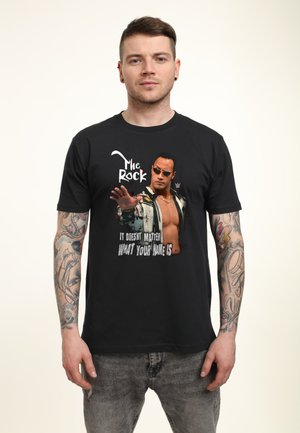 Zwart T-shirt met een afdruk van een gespierd figuur met een zonnebril, tekst met "The Rock" en "Het maakt niet uit hoe je heet."