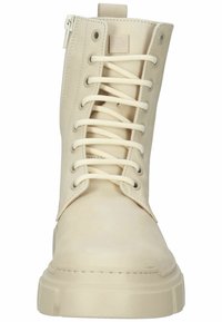 Botte de combat crème à lacets avec semelle épaisse et fermeture éclair latérale, vue de face sur fond blanc.