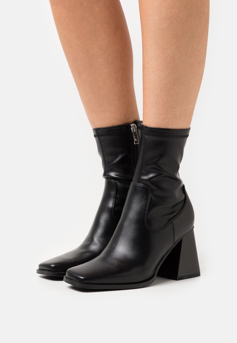 Bottes basses en cuir noir avec un design décontracté, un bout carré et un talon épais. Dotées d'une fermeture éclair latérale pour un accès facile et d'une couture texturée.