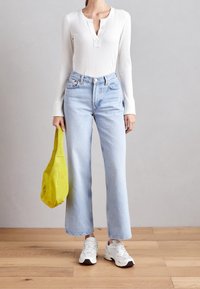 Vit ribbad långärmad topp, ljusblå högmidjade jeans, färgglad gul väska och vita sneakers med grå detaljer.