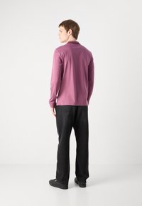 Camisa de manga longa, lilás claro, com colarinho, usada com calças largas pretas e sapatos pretos, exibindo uma textura suave e mate.