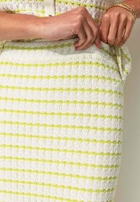 Jupe en tissu texturé blanc avec des rayures horizontales jaunes et une coupe ajustée, avec des coutures visibles et un détail de ceinture.