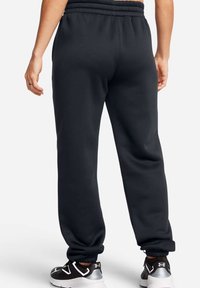 Pantalones deportivos negros con cintura elástica y tobillos ajustados. Textura suave y corte relajado, mostrados por la parte de atrás sin logotipos visibles.