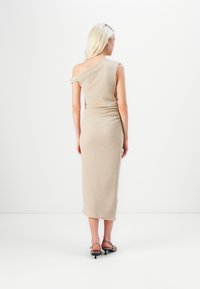 Beige, yhden olkapään mekko, jossa on istuva siluetti, rypistyneet sivudetailit ja hienovarainen tekstuuri, yhdistettynä remmineuloksiin.