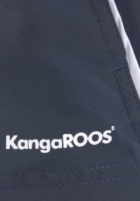 Tissu marine avec une finition texturée mettant en avant un logo "KangaROOS" blanc. Le design comprend des coutures visibles et un panneau latéral contrastant.