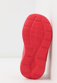 Semelle de chaussure de sport rouge avec un design texturé. Comprend un motif hexagonal, des crans pour la traction, et un détail de logo au centre.