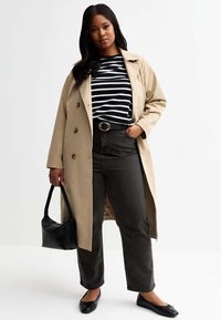 Beige trench coat med stora knappar, svart och vitrandig skjorta, mörka jeans, svarta ballerinaskor och en liten svart handväska.