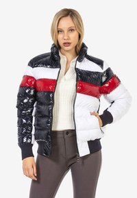 Pufferjacke mit glänzender Oberfläche, mit horizontalen Streifen in Schwarz, Weiß und Rot. Stehkragen und gerippte Bündchen.