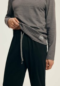 Graues Langarmshirt mit weißen Streifen und Etikett, kombiniert mit schwarzen Hosen mit Kordelzugbund und glatter Textur.