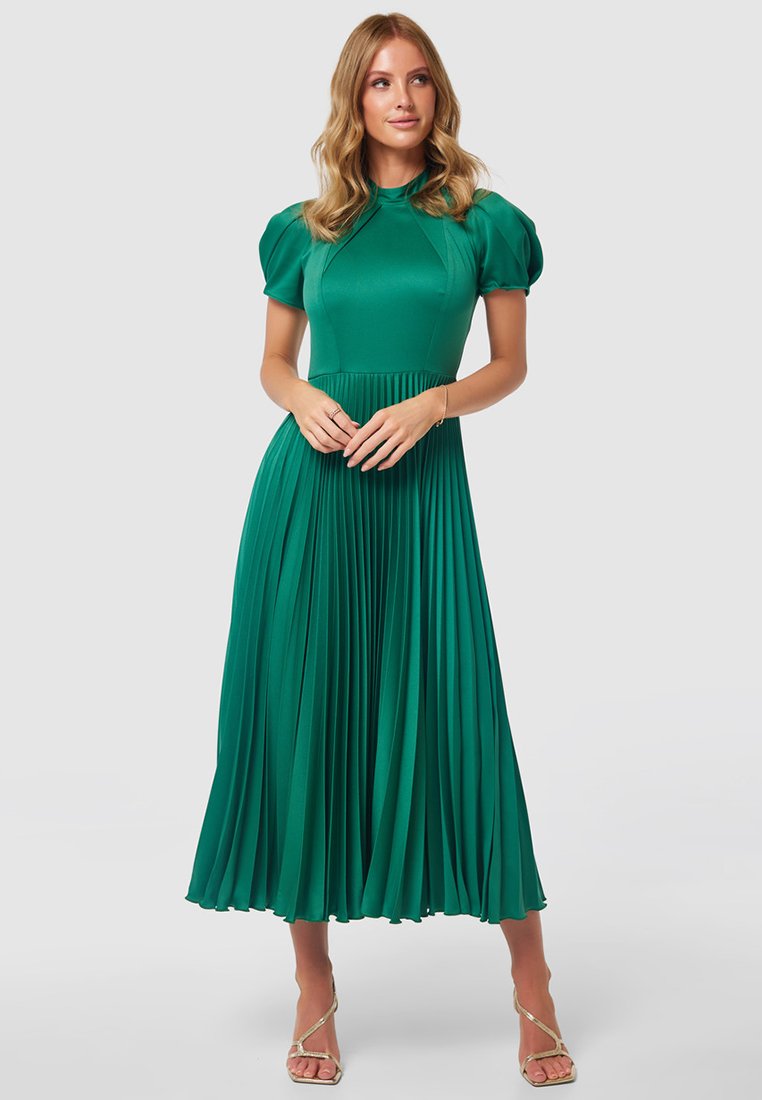 Zielona, plisowana midi sukienka z bufkami i dopasowanym gorsetem. Gładka faktura i okrągły dekolt. Modelka pozowała z dłońmi złożonymi.