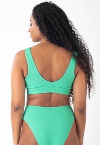 Reggiseno bikini verde a coste con spalline larghe e schiena bassa a scollatura, abbinato a un slip a vita alta. Tessuto testurizzato con design senza cuciture.